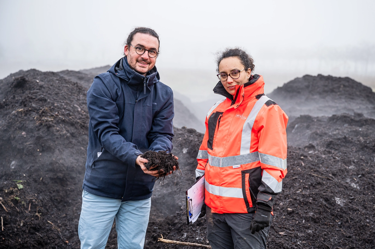 Une photo de deux personnes devant un site de compostage