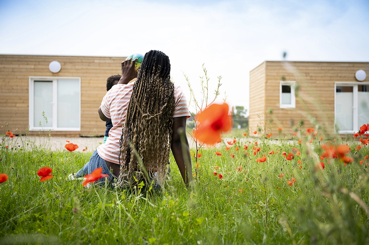 une mère et son enfant assis dans l'herbe devant les Tiny Houses à la saulaie, Oullins